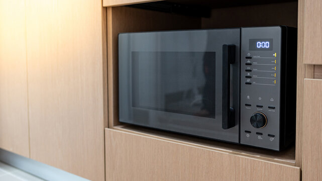 Modern black microwave oven in wooden cabinet. Home appliance in the kitchen