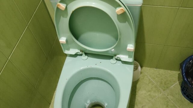 Unclean green toilet with open seat, urine and fecal stains in a tiled bathroom