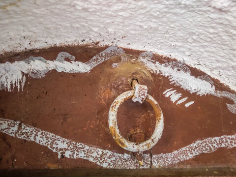 Weathered iron ring mounted on a rustic brown wall with textured white paint accents captures historical charm in close up view for architectural or heritage photography.