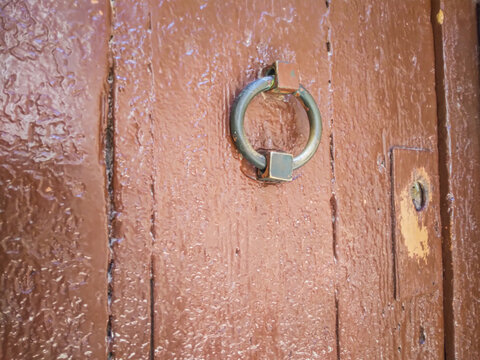 Antique iron ring door knocker mounted on a textured rustic brown wooden surface captured in a close up perspective highlighting weathered craftsmanship and vintage home design