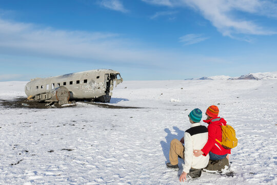 Young adventurous couple  sitting and watching for on Solheimasandur plane in winter in Iceland
