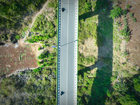 Aerial view of Jembatan Tepus Baru bridge spanning over lush green vegetation with a long shadow cast on the ground in Kecamatan Tepus, Daerah Istimewa Yogya, Indonesia.