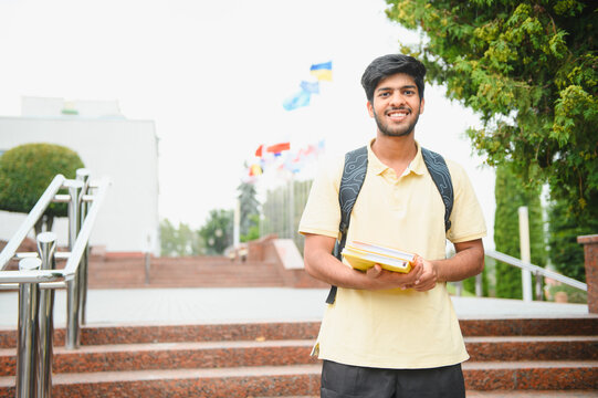 Young indian student smiling holding books on campus