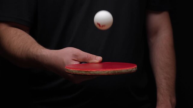 Moscow, August 10, 2026, Hand holds red ping pong paddle. White ball hovers mid-air. Black backdrop emphasizes the action. Perfect for sports training content. Ideal for reflex demonstrations. Great