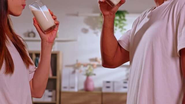 Couple holding milk glass drink at home kitchen interior hand lifestyle beverage toast healthy dairy refreshment casual indoor morning routine white shirt warm mood relaxed breakfast moment