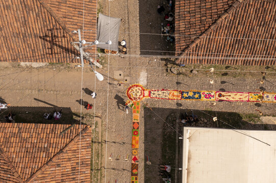 Aerial view of the intricate Patamban floral rug on a cobblestone street, surrounded by terracotta-tiled rooftops and people observing the colorful patterns in Patamban, Michoacan, Mexico.