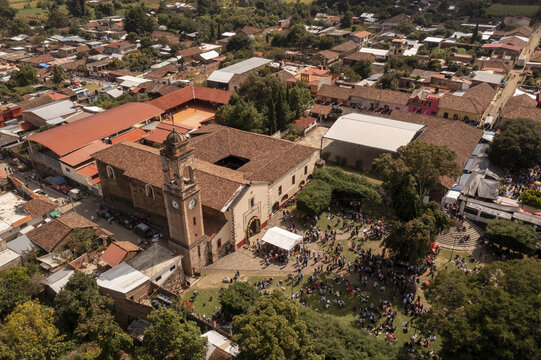 Aerial view of the Patamban floral rug displayed in the town square with a historic church, surrounding rooftops, and people gathering in Patamban, Michoacan, Mexico.