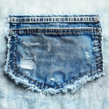 close-up of a worn frayed blue denim back pocket with distressed holes, visible stitching and textured faded fabric evoking casual nostalgic wear