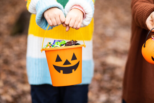 Kid child in a colorful striped sweater holds a Halloween pumpkin bucket filled with candy