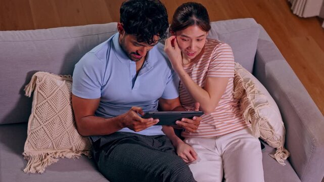 Couple using tablet on sofa at home in living room with smile together enjoying leisure technology digital screen conversation cozy interior scene
