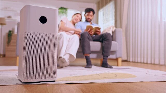 Air purifier couple reading book on sofa in living room home interior clean appliance foreground indoor filter relaxing comfort soft apartment setup