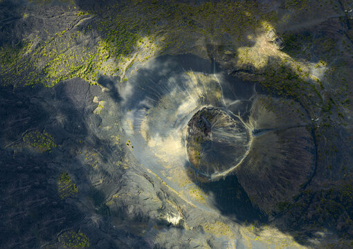Aerial view of the Paricutin volcano crater surrounded by dark volcanic lava fields and patches of green vegetation under cloud shadows in San Juan Parangaricutiro, Michoacan, Mexico.