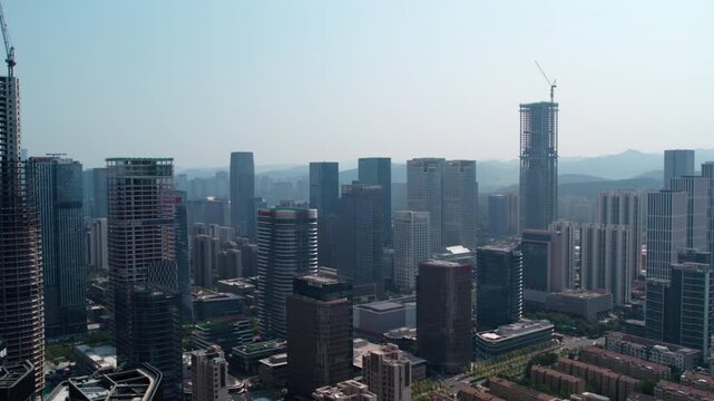 A panoramic aerial view of a modern urban skyline with numerous tall buildings, some under construction, set against distant mountains.