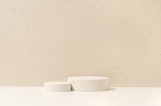 Two White Cylinder Podiums of Different Heights on White Shelf Against Travertine Wall Background