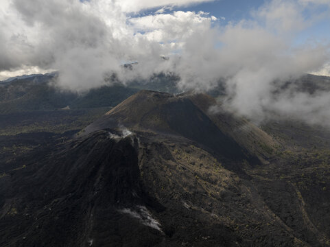 Aerial view of Paricutin volcano with its dark volcanic slopes, rugged lava fields, and wispy clouds drifting over the crater in San Juan Parangaricutiro, Michoacan, Mexico.