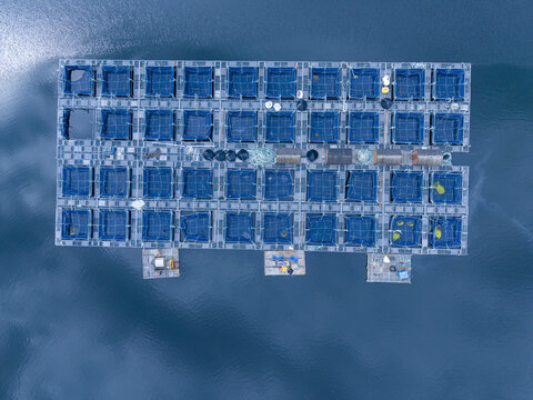 Aerial view of a fish farm with blue net cages floating on the water in Lochailort, Scotland, United Kingdom.