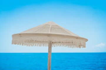 Minimalist woven beach umbrella against a vibrant blue sea and sky © Yana Slavova