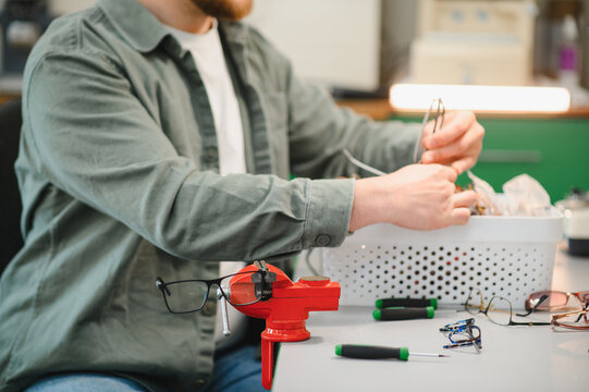 Optician repairing eyeglasses using tools at small workbench