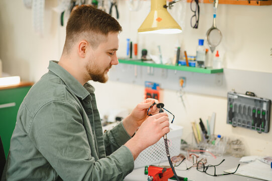 Optician repairing eyeglasses frame using precision tools in a workshop