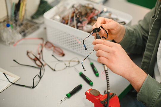 Optician hands repairing eyeglasses using precision tools at workbench