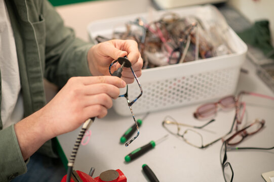 Practitioner repairing broken eyeglasses frames in optics workshop