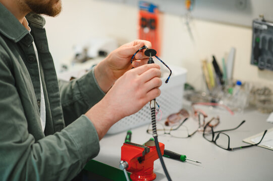 Optician repairing broken eyeglasses in workshop with tool