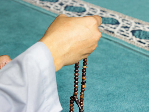 Close up of asian man hands who is praying with a tasbih for dzikir, religion and faith concept, close up