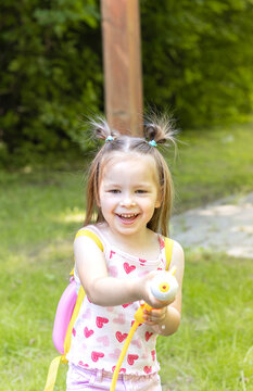 Young girl with pigtails wearing a heart-patterned tank top holds a water gun while playing in a green backyard on a sunny day