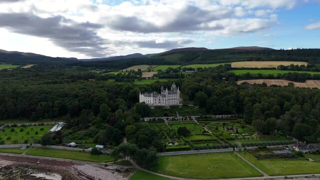 Drone shot over Dunrobin Castle estate in Golspie featuring fairytale conical spires, Victorian style parterre gardens, and countryside forest scenery in Sutherland Scotland