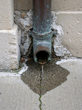 Water dripping from old copper drainpipe into puddle on stone pavement