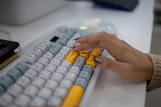 Close-up of woman typing on colorful mechanical keyboard at an office desk, representing computer work, digital productivity, technology, data entry and modern workplace tasks.