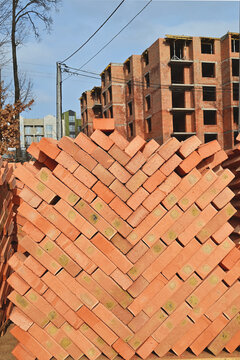 Close-up view of red clay bricks stacked on wooden pallets at a construction site, creating a repeating geometric pattern