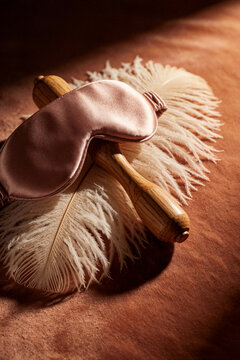 Silk sleep mask and wooden feather duster on warm textured background