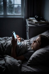 Fototapeta premium Teenager lying in bed using smartphone at night, blue light from screen