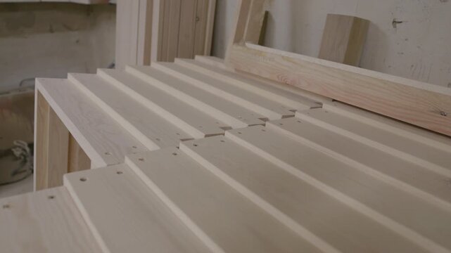 Rows of unfinished wooden boards and slats with drilled holes arranged for assembly in a carpentry workshop, showing natural grain and furniture production