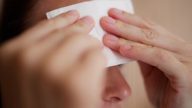 Close-up of woman wiping sweat from her forehead with a tissue, feeling hot and uncomfortable during a summer heatwave, illustrating extreme heat, high temperature and overheating