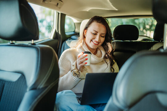 Woman working remotely with laptop and coffee in car