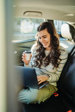 Young woman working on laptop in car back seat