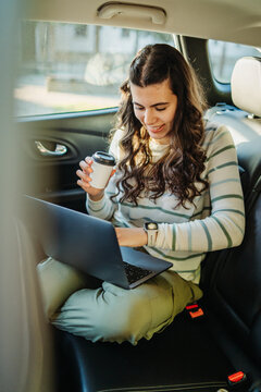 Woman working on laptop and drinking coffee in car