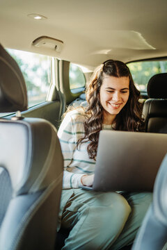 Woman smiling while working on laptop in car