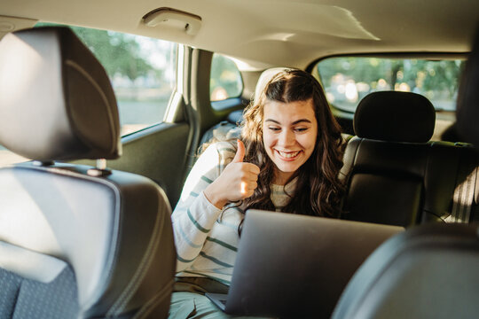 Woman working on laptop giving thumbs up in car