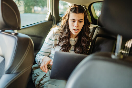 Woman working on laptop in car backseat