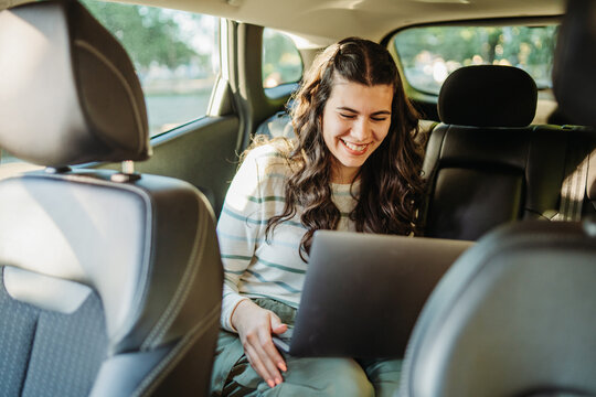 Woman smiling using laptop in car back seat