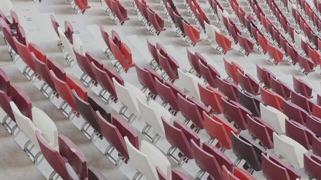 Diagonal panning shot of empty red and white seats in a large stadium or arena. The bleachers are ready for spectators at a major event