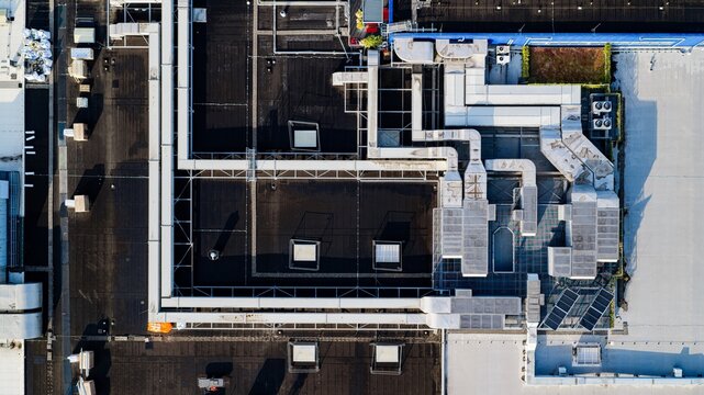 Aerial view of an industrial rooftop featuring complex HVAC ducting systems, skylights, and solar panels on a flat roof surface in Delft, South Holland, Netherlands.