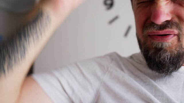 Bearded man smelling his t-shirt and reacting with disgust to unpleasant body odor from sweaty underarms, illustrating excessive perspiration, personal hygiene and summer heat