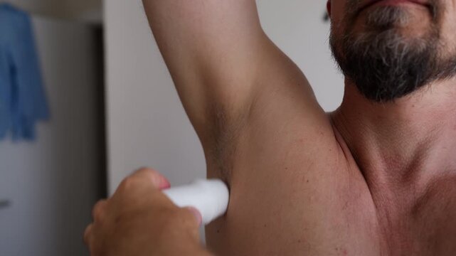 Shirtless man applying roll-on deodorant to his underarm, demonstrating daily freshness and protection against sweat and unpleasant body odor.
