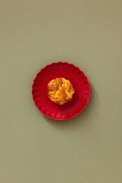 Top view minimal studio photo of a Swedish cardamom bun topped with pearl sugar on a red scallop plate, centered on a sage green background with copy space. Ideal for bakery and fika concepts.
