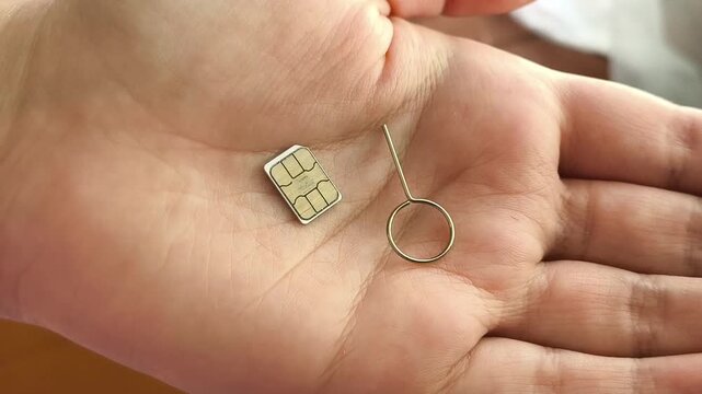 SIM card and SIM ejector tool held in hand close up, mobile connectivity, cellular network and mobile internet concept.
