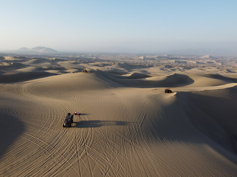 Aerial view of Huacachina sand dunes with dune buggies driving across the vast desert landscape in Ica, Ica, Peru.